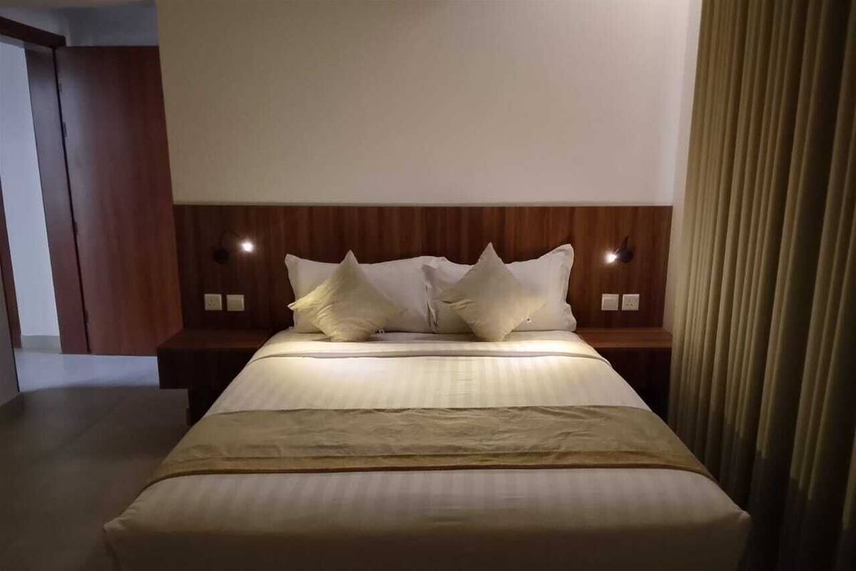 A hotel room with a large bed, wooden headboard, two bedside tables, and a curtain on the right.