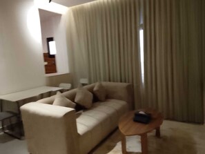 Una sala de estar con sofá, una mesita redonda y un ventanal con cortinas.