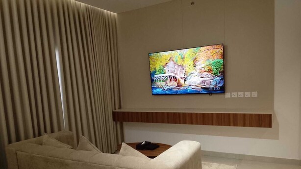 A modern living room with a flat-screen TV mounted on the wall, a beige sofa, and a wooden coffee table.