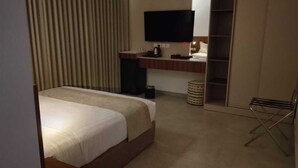 A hotel room with a bed, a television, a wardrobe, and a small table with a kettle.