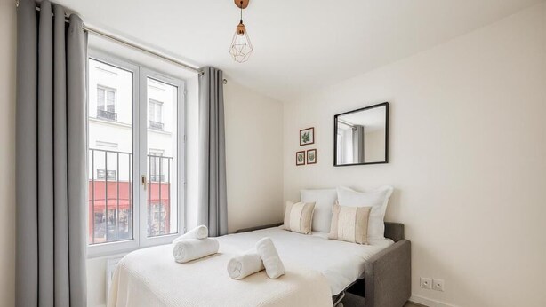 Un dormitorio con cama, una ventana con cortinas, un espejo y una lámpara.