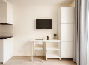A modern, minimalist room with a white desk, a flat-screen TV, and a small potted plant. - Studio cosy proche des Buttes-Chaumont (Paris)