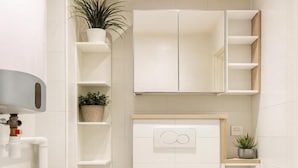 Baño pequeño con lavadora, inodoro y estanterías.