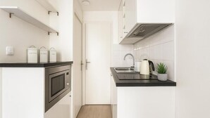 Cocina moderna con armarios blancos, encimera negra, microondas, hervidor y una planta en maceta.