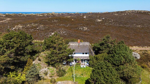 Ein Haus mit einem Strohdach, umgeben von üppiger Vegetation, mit freiem Blick auf die umliegende Landschaft und ein entferntes Gewässer.