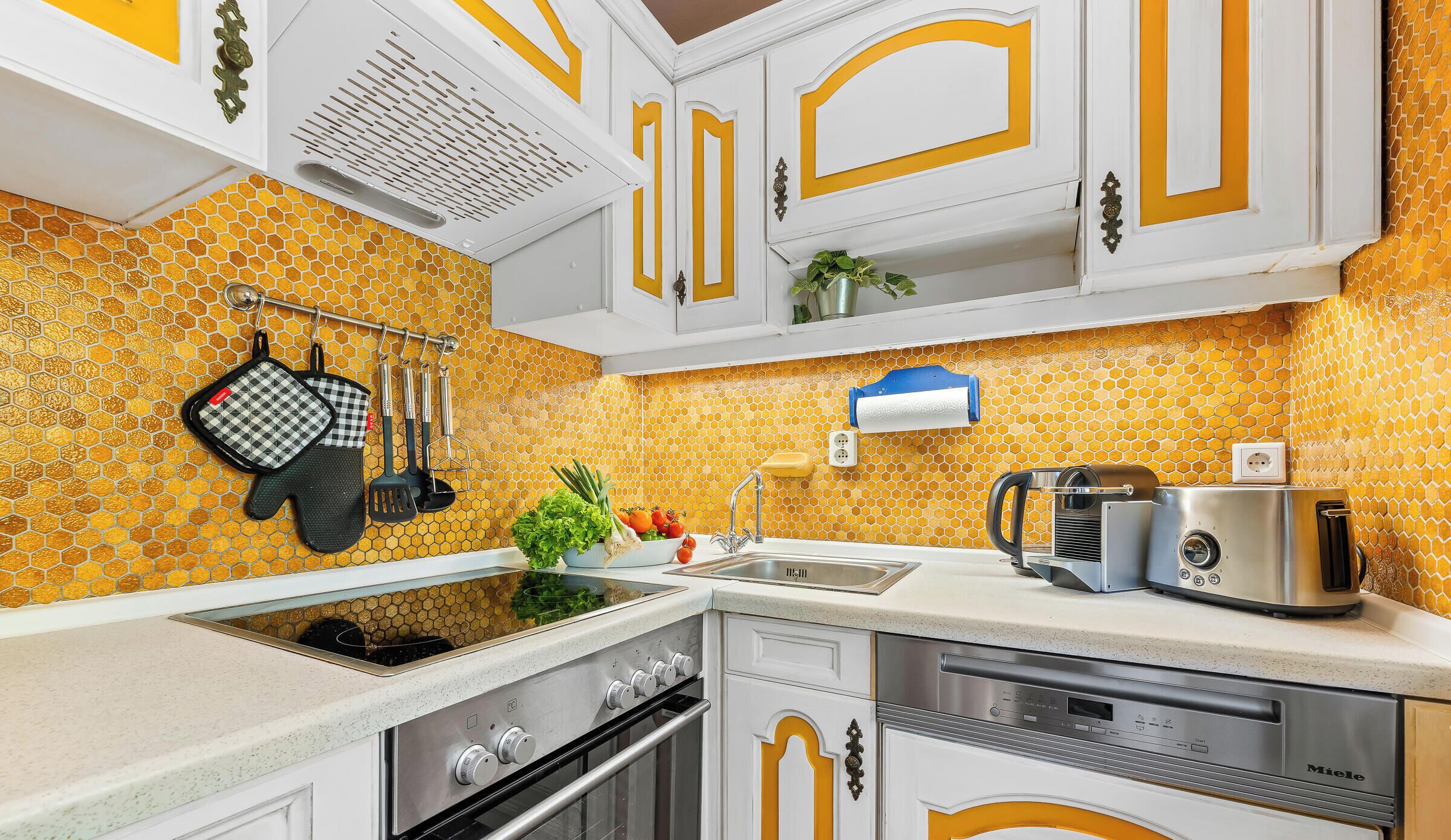 A kitchen with white cabinets, a stainless steel range hood, a sink, a coffee maker, and a dish rack.