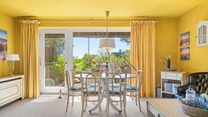 Ein Zimmer mit Esstisch, Stühlen, Lampe, Sofa und Blick durch eine Glastür.