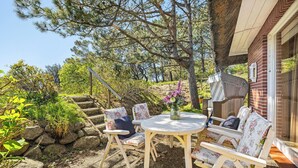 Eine Terrasse mit rundem Tisch und weißen Stühlen, umgeben von Grünpflanzen und einer Steinmauer.