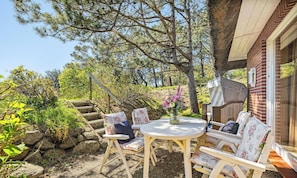 A patio with a round table and white chairs, surrounded by greenery and a stone wall. - The Yellow House in List on Sylt: Terrace, garden, and close to the beach—accommodates up to 3 people (List auf Sylt)
