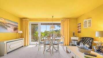 A room with a dining table, chairs, a sofa, a TV, and a window with curtains.