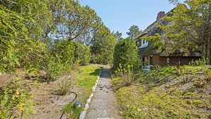 Ein rustikales Haus mit Strohdach, umgeben von üppiger Vegetation und einem Kiesweg, der dorthin führt.