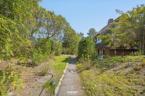A pathway leading to a thatched-roof house surrounded by greenery. - The Yellow House in List on Sylt: Terrace, garden, and close to the beach—accommodates up to 3 people (List auf Sylt)