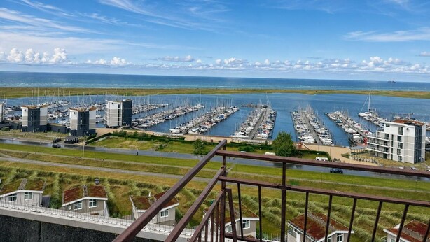 Una marina con numerose imbarcazioni ormeggiate, cielo sereno e vista sul mare.