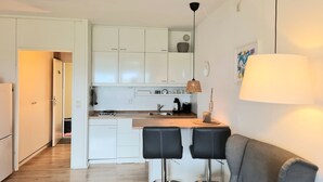 Una cucina compatta con mobili bianchi, una macchina da caffè e un'area pranzo con due sgabelli neri.
