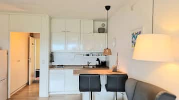 Uma cozinha compacta com armários brancos, uma cafeteira e um espaço de refeições com dois banquetes pretos.