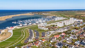 Vista aerea di una marina costiera con numerose imbarcazioni, edifici residenziali e una limpida visuale del mare.