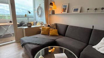 Uma sala de estar moderna com um sofá seccional, uma mesa de centro de vidro e vista através de grandes janelas.