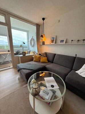 A modern living room with a sectional sofa, a glass coffee table, and a view through large windows.