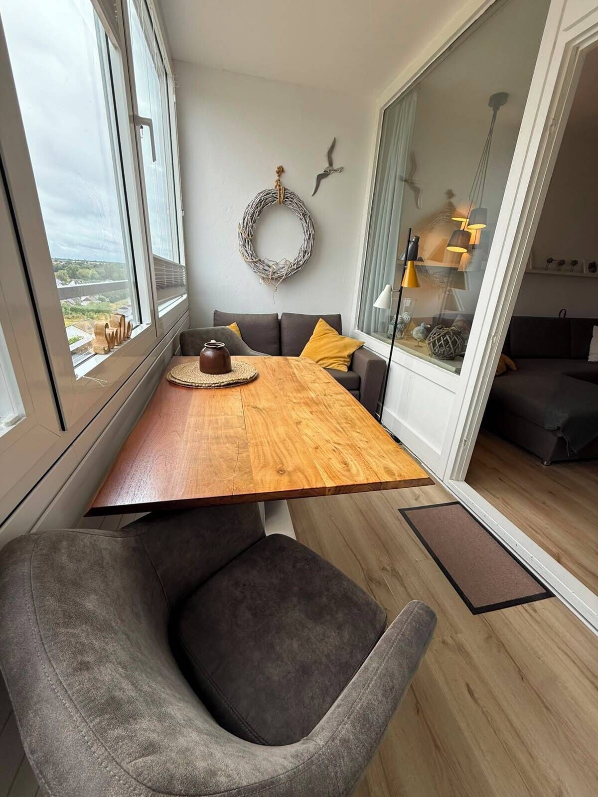 A modern dining area with a wooden table, grey upholstered chairs, a grey sofa, and a view through a glass door.