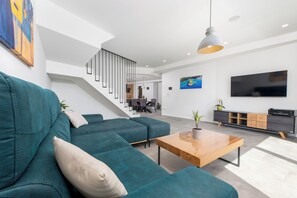 A modern living room with teal sofas, a wooden coffee table, a TV, and a staircase leading to a dining area. - Holiday Home Šime (Brela)