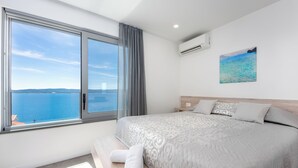 Ein Schlafzimmer mit großem Fenster, einem Bett, einem Nachttisch und einer Wand-Klimaanlage.