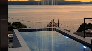 Ein moderner Infinity-Pool mit freiem Blick auf ein großes Gewässer und ferne Hügel.