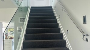 Een moderne trap met glazen balustrades en donkere, beklede treden.
