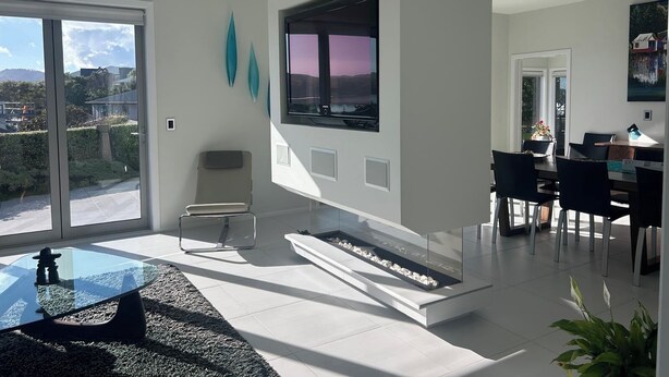 Een moderne woonkamer met een glazen salontafel, een open haard, een eethoek met stoelen en een groot raam met uitzicht.