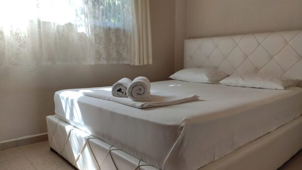 Cama bem arrumada com toalhas dobradas, cabeceira e janela com cortinas leves.