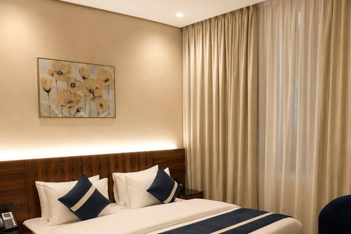 Habitación de hotel con una cama grande, cabecera, mesita de noche con teléfono, una silla, alfombra estampada y un cuadro en la pared.