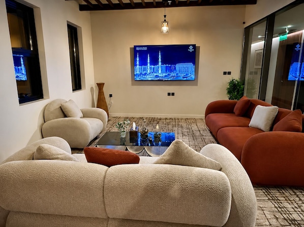 A modern living room with a large flat-screen TV, plush sofas, a coffee table, and a patterned rug.