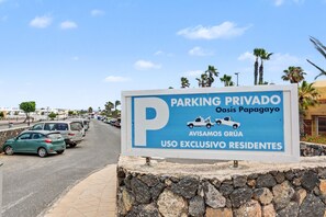 A sign indicating private parking at Oasis Papagayo, with a stone wall and parked cars. - Vacation Apartment 'Oasis Papagayo Cozy Patio' with Shared Pool, Private Terrace and Wi-Fi (Corralejo)