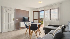 Ein modernes Wohnzimmer mit grauem Sofa, einem Esstisch mit Stühlen, einem Fernseher und einem Balkon mit Blick.