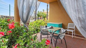 Eine Terrasse mit Tisch und Stühlen, einem türkisblauen Schrank und einer weißen Bank unter einer Markise.