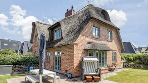 A house with a thatched roof, brick walls, and a patio with outdoor furniture. - Wääfblik – Your vacation home on Sylt with a sauna and ocean view (Wenningstedt-Braderup (Sylt))