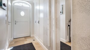 A hallway with a white door, a black mat, and patterned wallpaper. - Wääfblik – Your vacation home on Sylt with a sauna and ocean view (Wenningstedt-Braderup (Sylt))