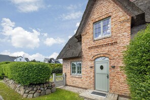 Ein Backsteinhaus mit Strohdach, einer Steinmauer und einem gepflegten Heckenbewuchs.