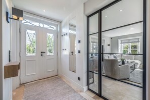 Ein modernes Interieur mit einer doppelten Tür, einem großen Spiegel, einem gemusterten Teppich und Blick auf einen Wohnbereich mit Sofa und Pflanze.