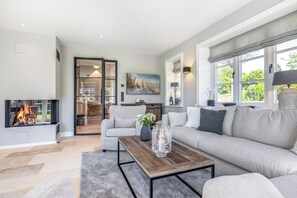 Ein modernes Wohnzimmer mit Kamin, einer Couch, einem Couchtisch und Blick ins Freie.