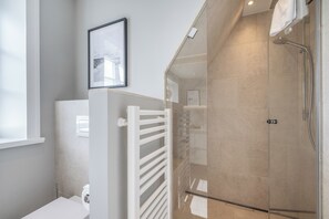 Ein modernes Badezimmer mit einer Duschkabine aus Glas, einem weißen Heizkörper und einem gerahmten Bild an der Wand.