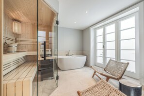Ein modernes Badezimmer mit einer freistehenden Badewanne, Holzbanken und großen Fenstern.