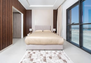 A modern hotel room with a large bed, a view of the beach, and a wooden panel wall.