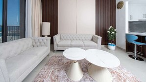 A modern living room with a sofa, two coffee tables, a potted plant, and a view of the kitchen. - Seafront Apt w/ Pool & Gym near Attractions (Sharjah)