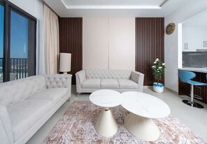 A modern living room with a sofa, two coffee tables, a potted plant, and a view of the kitchen. - Seafront Apt w/ Pool & Gym near Attractions (Sharjah)