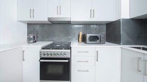 A modern kitchen with white cabinets, a stove, oven, microwave, and toaster. - Seafront Apt w/ Pool & Gym near Attractions (Sharjah)