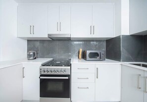 A modern kitchen with white cabinets, a stove, oven, microwave, and toaster. - Seafront Apt w/ Pool & Gym near Attractions (Sharjah)