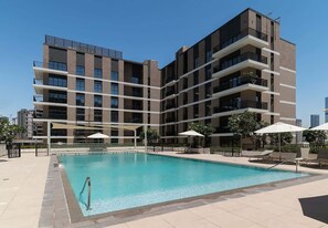A modern building with a swimming pool, outdoor seating, and a clear sky. - Seafront Apt w/ Pool & Gym near Attractions (Sharjah)
