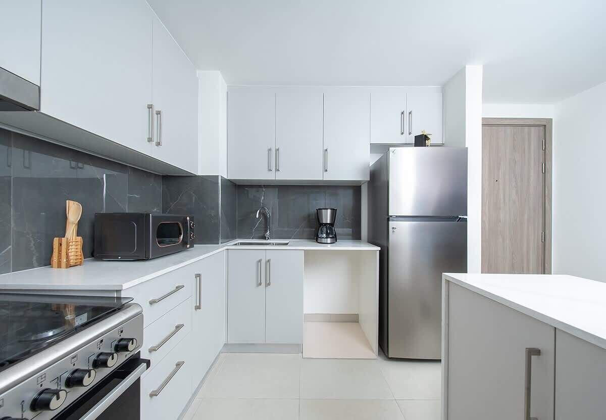 Una cocina moderna con armarios blancos, un refrigerador de acero inoxidable, un microondas y una estufa.