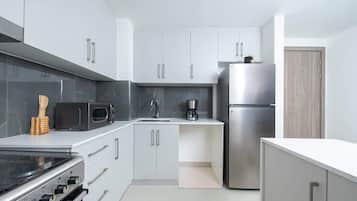 Una cocina moderna con armarios blancos, un refrigerador de acero inoxidable, un microondas y una estufa.