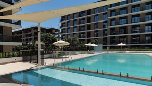 A swimming pool with a clear blue water surface, surrounded by a covered deck area with umbrellas. - Seafront Apt w/ Pool & Gym near Attractions (Sharjah)